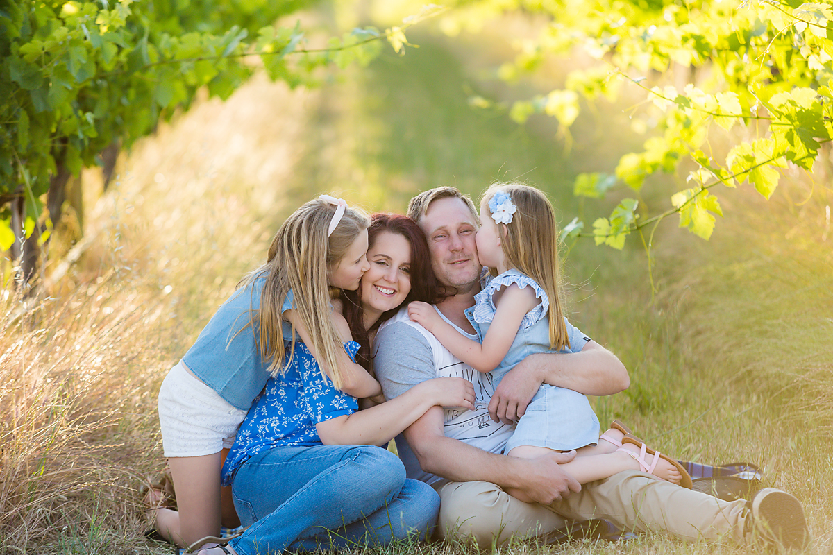 mum and dad and their  two children laughing and smiling on a rug in the vineyards at their family photo session by deb elton photography