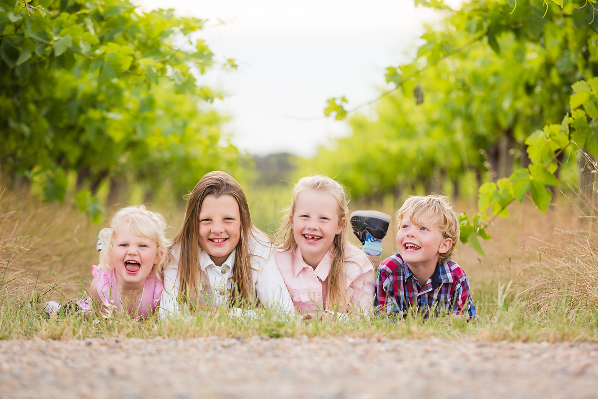 kids on their tummies smiling at their family photo session in the vineyards by deb elton photography